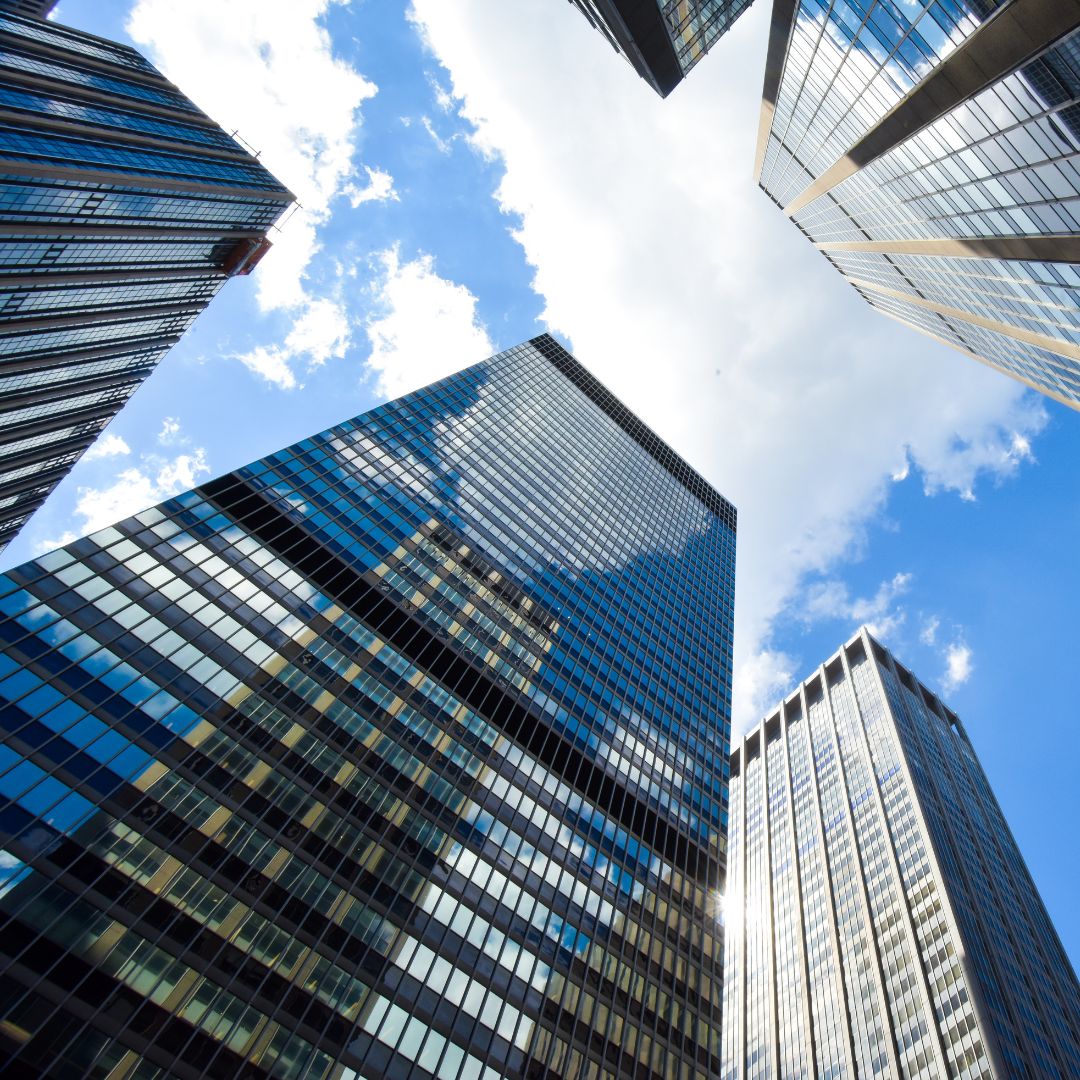 Upward view of modern glass and steel skyscrapers symbolising the headquarters of listed corporations and multinational groups.